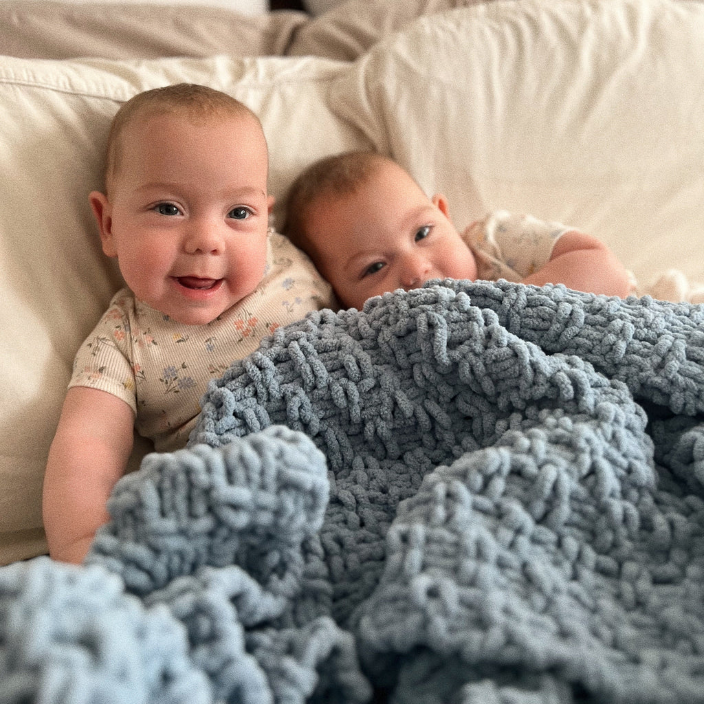 two babies with blue knit blanket on pillows