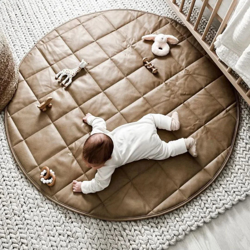 Baby lying on a round quilted mat with toys in a nursery setting