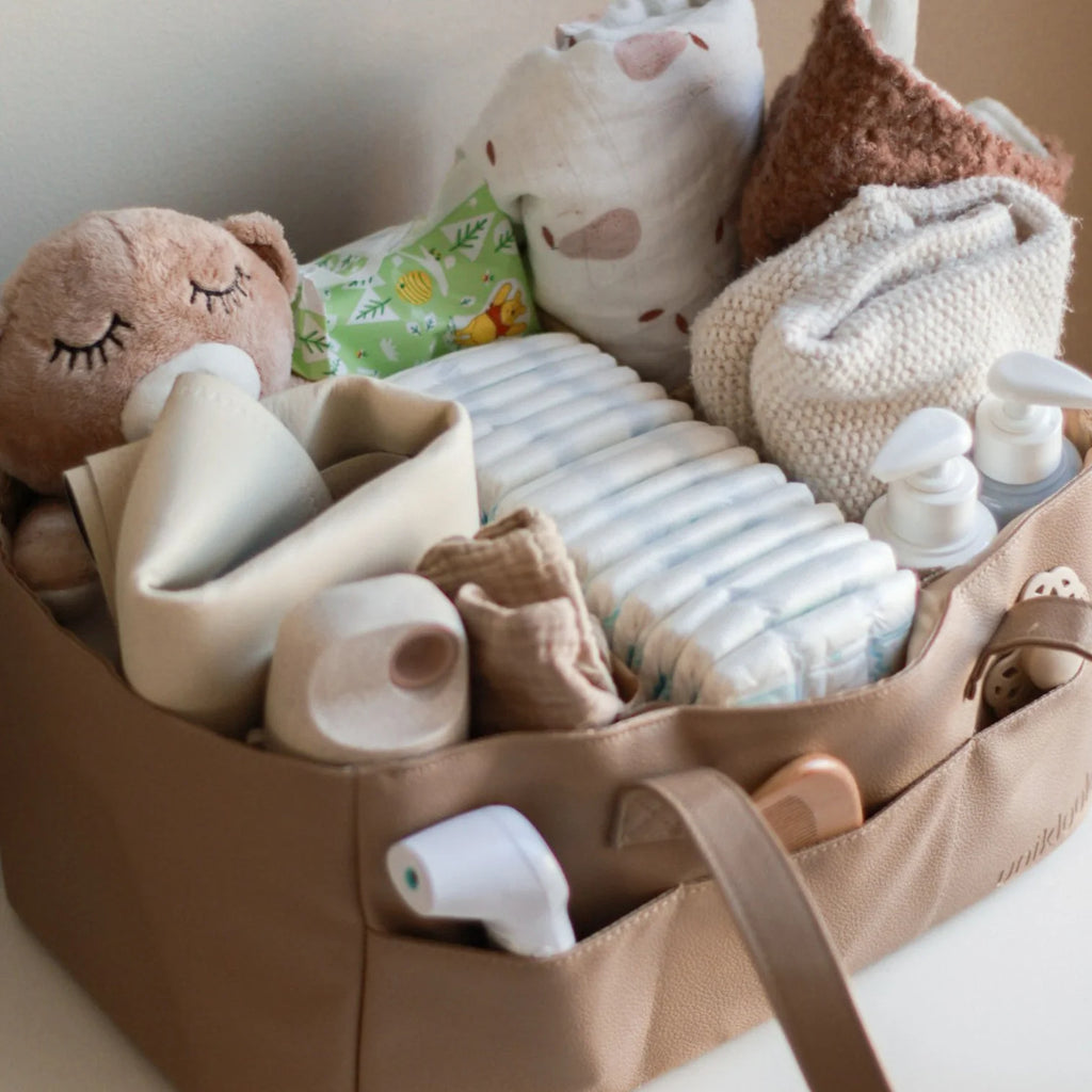 Baby care items including diapers, bottles, and toys in a brown bag on a light background